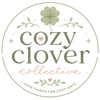 A circular logo or label reading 'cozy clover collective' with a four-leaf clover at the top, delicate floral accents, small pink hearts, and the phrase 'CUTE THINGS FOR COZY DAYS' on a white background.